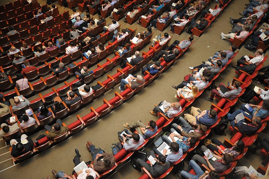 Foto: Sitzreihen mit vielen Personen in einem Konferenzsaal von oben betrachtet